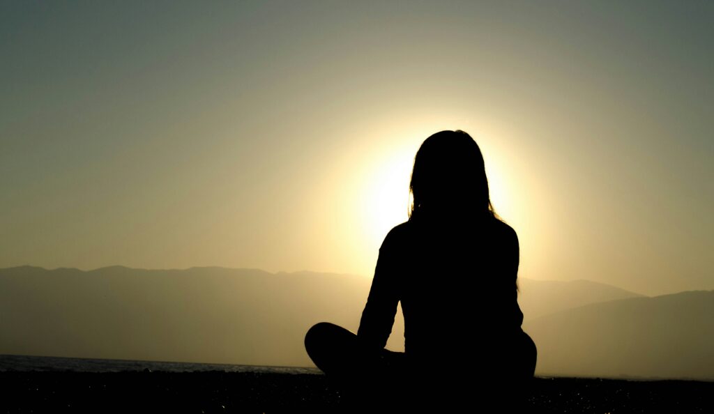 Person sitting in silhouette at sunset, representing overthinking and rumination